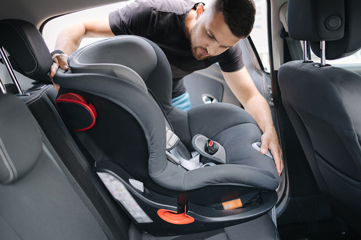 Man installs a child car seat in car at the back seat.